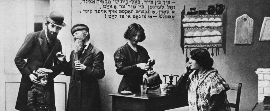 A shadchan and another man have a conversation while a woman pours from a teapot. The shadchan, or marriage broker, was traditionally an essential part of a Jewish marriage.