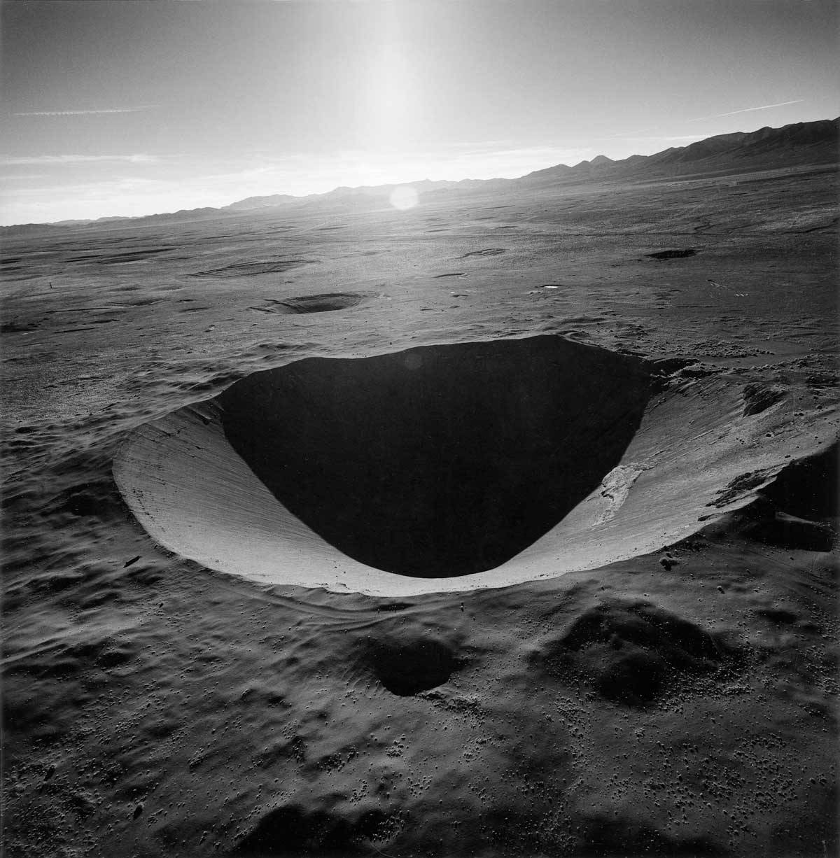 Emmet Gowin, SEDAN CRATER, NORTHERN END OF YUCCA FLAT, NEVADA TEST SITE, 1996. Part of Operation Plowshare, the Sedan test was intended to develop peaceful uses for nuclear weapons. On July 6, 1962, the Sedan device exploded with a yield of 104 kilotons, similar to the warhead of the Minuteman I missile. Sedan was buried only 635 feet below the surface. The blast produced a crater approximately 1,200 feet wide and 330 feet deep, displacing 12 million tons of earth and releasing high levels of radiation into the atmosphere. (From THE NEVADA TEST SITE by Emmet Gowin, with a foreword by Robert Adams, Princeton University Press, 2019.)