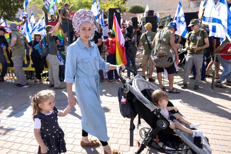 A religious woman walks with her children past Israeli activists protesting in front of Har Hamor Yeshiva, a religious seminary in East Jerusalem's Har Homa neighborhood, on July 30, 2023