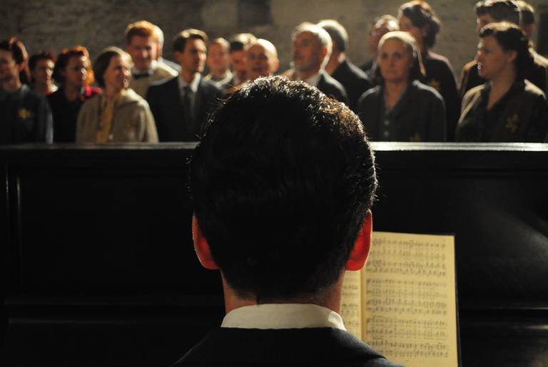 A scene from the documentary Defiant Requiem: Voices of Resistance re-enacting Raphel Schacter playing piano in front of the Terezin Choir. (Partisan Pictures)