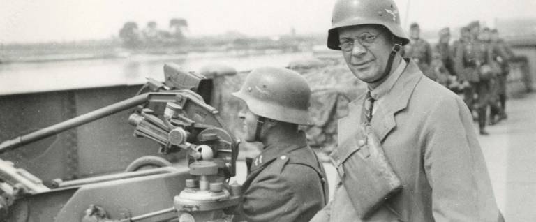 AP Berlin bureau chief Louis P. Lochner, somewhere in Germany, stands next to a Nazi soldier seated in a piece of artillery.