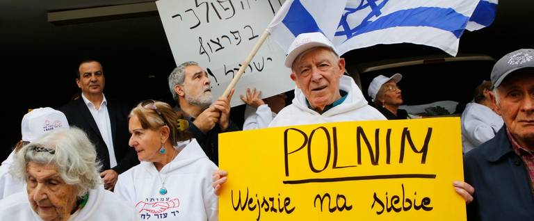 Holocaust survivors hold banners and wave an Israeli flag during a protest in front of Polish embassy in Tel Aviv on February 8, 2018, against a controversial bill passed by the eastern European country's senate. The legislation sets fines or a maximum three-year jail term for anyone describing Nazi German death camps in Poland, like Auschwitz-Birkenau, as Polish.
