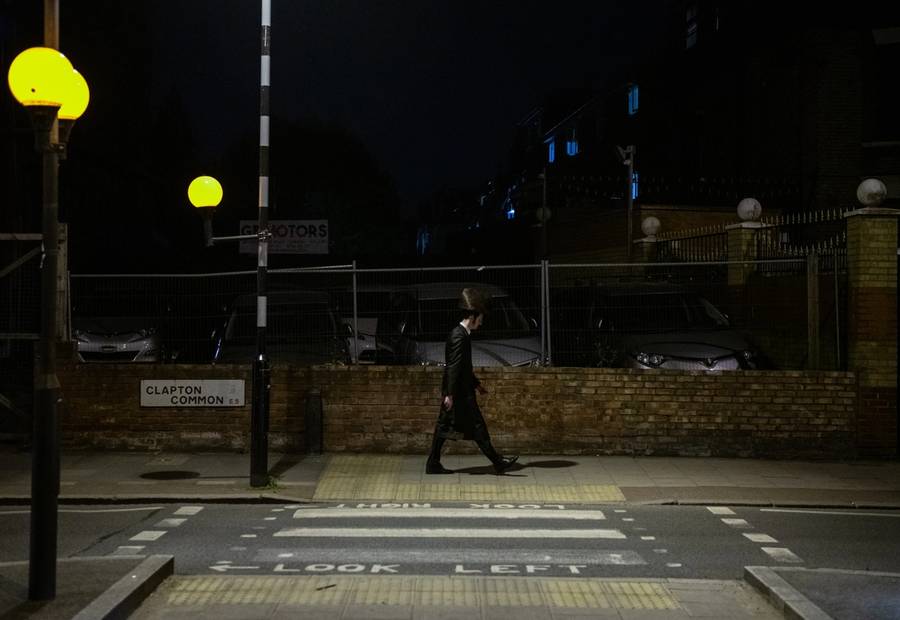A Hasidic Jewish man walks past a pedestrian crossing at nighttime in Stamford Hill, London, on May 9, 2020