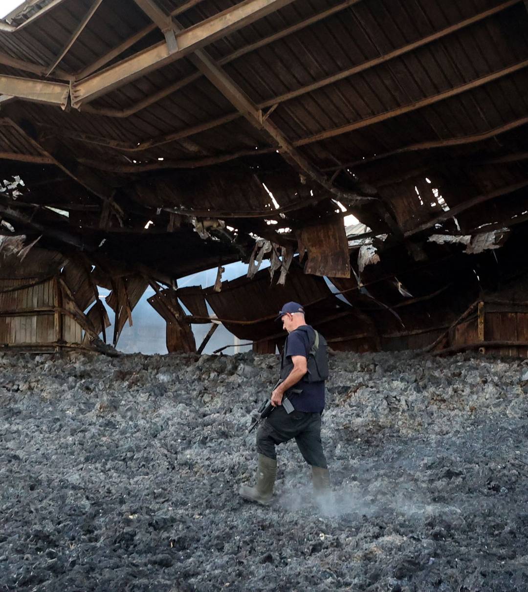 An armed resident walks amid the ashes of a heavily damaged building in kibbutz Alumim, following the October 7 attack by Hamas fighters, in southern Israel near the Gaza Strip on October 18, 2023