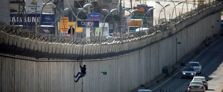 A Palestinian man uses a rope to climb over a section of Israel's controversial separation barrier that separates the West Bank city of al-Ram from East Jerusalem, February 24, 2016. 