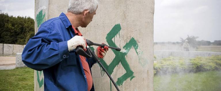 A man uses a pressure hose to clean the monument with Nazi swastikas painted over it in Jedwabne, September 1, 2011. Vandals daubed Nazi swastikas and SS signs on a monument in the town of Jedwabne, eastern Poland, which commemorates the mass killing of Jews burned alive by their Polish neighbors during World War II.