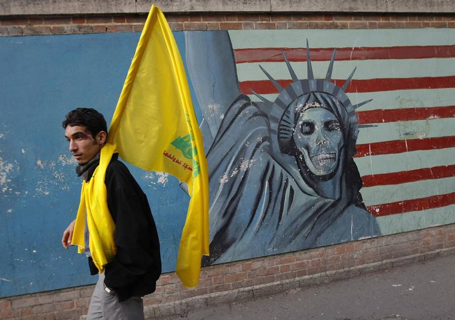 An Iranian man holding a Lebanese Hezbollah flag walks past a mural on the wall of the former U.S. Embassy in Tehran on Jan. 20, 2009