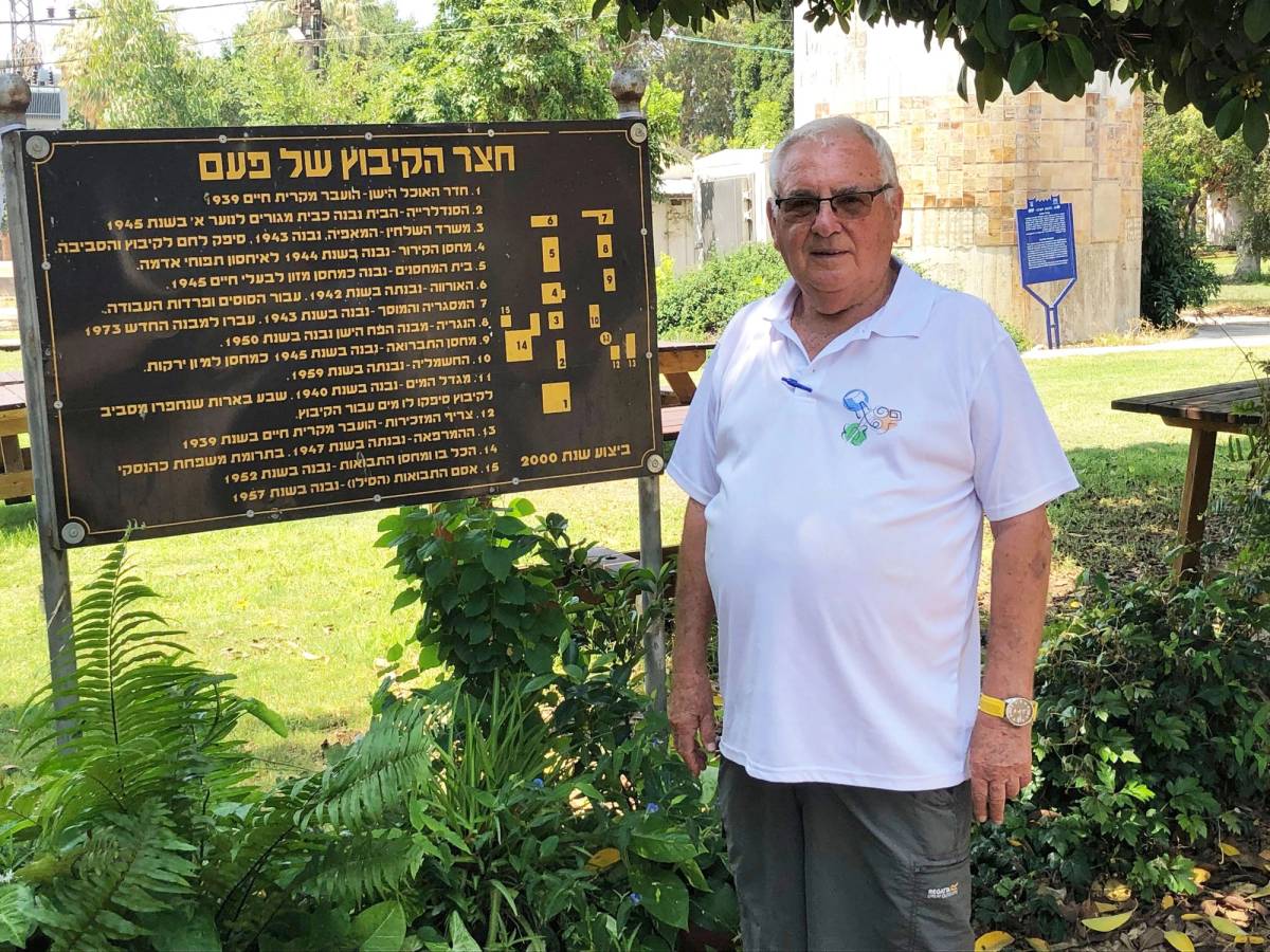 Benny Barak stands at a sign that directs visitors to historical buildings clustered at the kibbutz. No. 11 is the water tower, built in 1940, looming behind him.