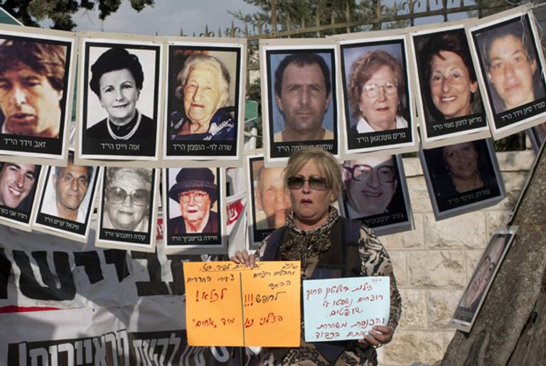 An Israeli woman holds signs in front of pictures of Israelis who were killed by Palestinians militants during a protest against the release of Palestinian prisoners in front of the Prime Minister's Residence in Jerusalem, on April 1, 2014. (AHMAD GHARABLI/AFP/Getty Images)