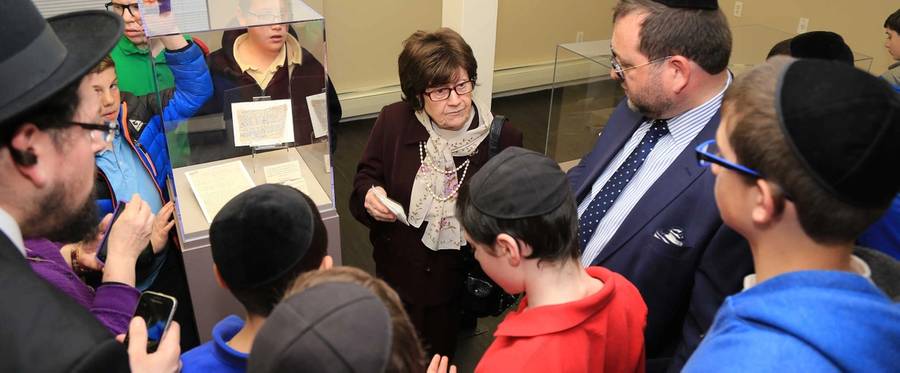 Mrs. Sara Seidman, wife of the late Dr. Hillel Seidman, seen here talking to school children about a cloth (displayed) upon which her husband wrote a plea for rescue and which was smuggled out of the Vittel internment camp. Dr. Seidman was an archivist, researcher, and author. He kept a  diary (also in collection) chronicling the final days of the Warsaw Ghetto.