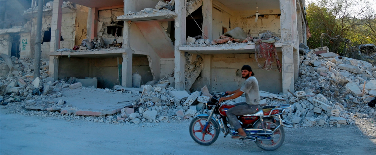 A Syrian man rides a motorcycle past a destroyed building in an area that reportedly was hit by an air strike in the district of Jisr al-Shughur, in Idlib province, on Sept. 4, 2018.
