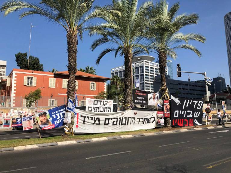 Placards and banners amid the palm trees on the Kaplan Street traffic island, with the Defense Ministry building in the background