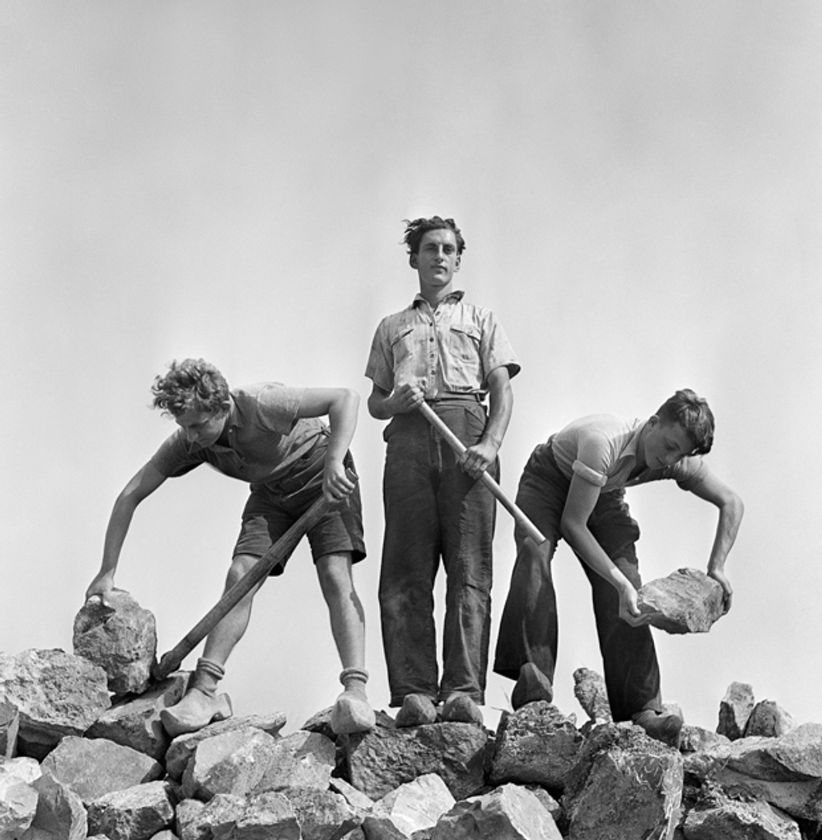 Roman Vishniac. [Ernst Kaufmann, center, and unidentified Zionist youth, wearing clogs while learning construction techniques in a quarry, Werkdorp Nieuwesluis, Wieringermeer, The Netherlands] 1939. © Mara Vishniac Kohn, courtesy International Center of Photography