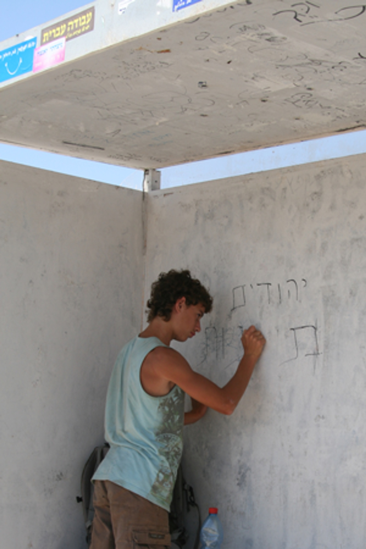 A hitcher tries to erase ‘Jews are sons of bitches’ from a bus stop and hitching stop at Tapuach junction, near Yitzhar. (Daniella Cheslow)
