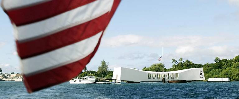 The U.S. flag waves in the wind from the back of a ferry as the USS Arizona Memorial looms in the background December 7, 2004 in Pearl Harbor, Hawaii. 
