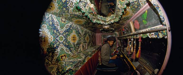 Linoleum patterned after oriental rugs surrounds driver of truck-bus, Afghanistan.