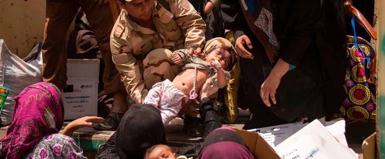 A member of the Iraqi forces carries a child, as women who fled the fighting with Islamic State (IS) group jihadists in the Old City of Mosul move their belongings prior to being relocated from the city's western industrial district on July 8, 2017.