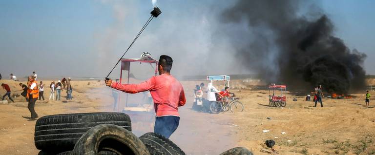 A Palestinian protester uses a slingshot to throw back a tear gas canister toward Israeli forces during clashes following a demonstration along the border east of Gaza City on July 6, 2018.