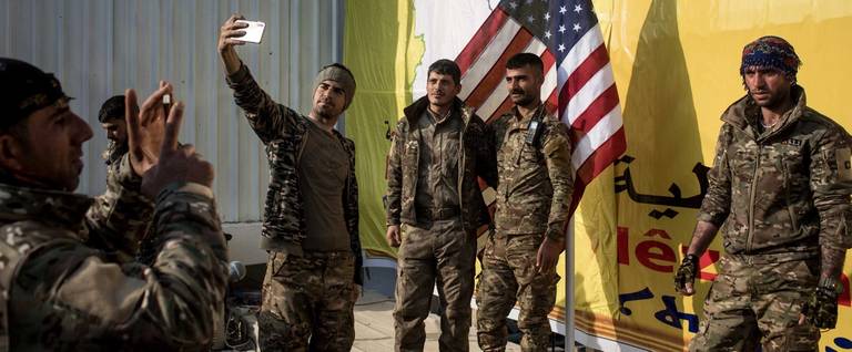 Syrian Democratic Forces (SDF) fighters pose for a photo with the American flag on stage after a SDF victory ceremony announcing the defeat of ISIL in Baghouz was held at Omer Oil Field on March 23, 2019 in Baghouz, Syria.