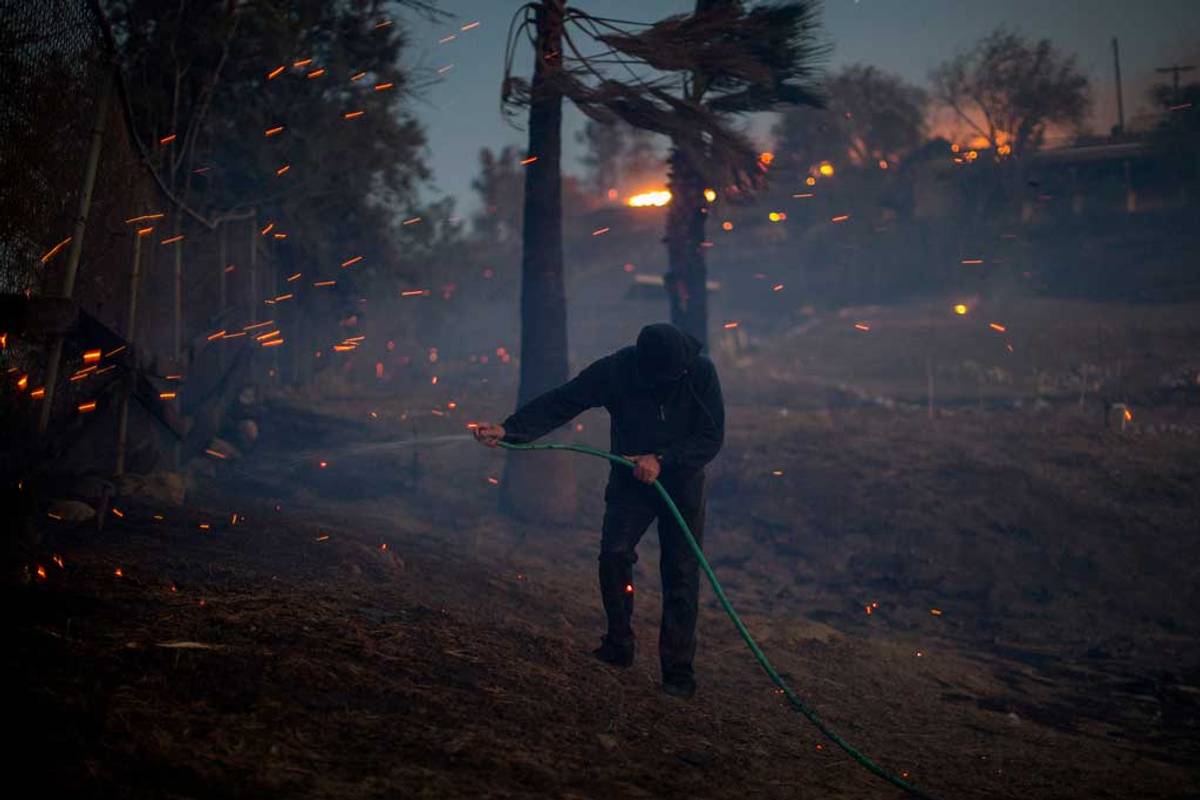 A strong wind blows embers around a resident hosing his burning property during the Creek Fire on Dec. 5, 2017, in Sunland, California. (Photo: David McNew/Getty Imagess)