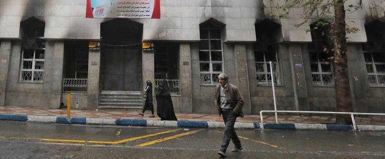 Iranians walk past a local bank branch that was damaged during demonstrations against petrol price hikes, on Nov. 20, 2019, in Shahriar, west of Tehran 
