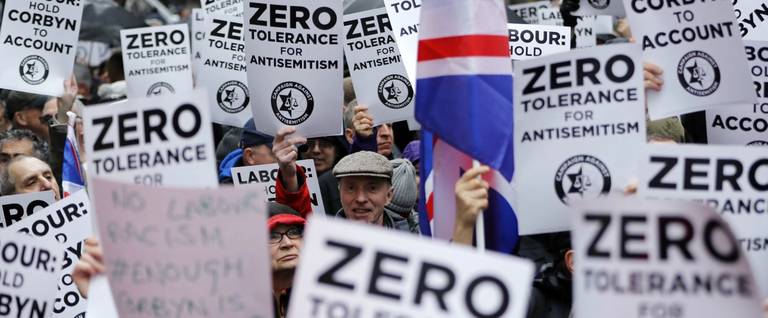 People hold up placards and union flags as they gather for a demonstration organized by the Campaign Against Anti-Semitism outside the head office of the British opposition Labour Party in central London on April 8, 2018.