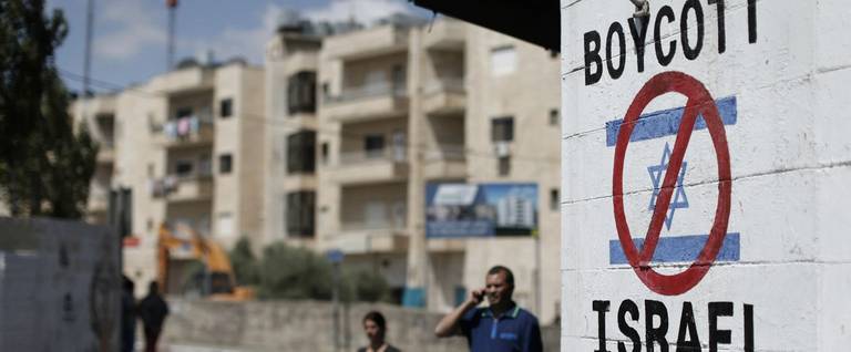 Palestinians walk past a sign painted on a wall in the West Bank biblical town of Bethlehem on June 5, 2015, calling to boycott Israeli products.