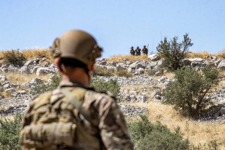 A Lebanese army soldier, at left, in Kfar Shouba in southern Lebanon looks on from his side of the border as Israeli soldiers stand opposite, in background, in the Israeli-annexed Golan Heights on July 20, 2023