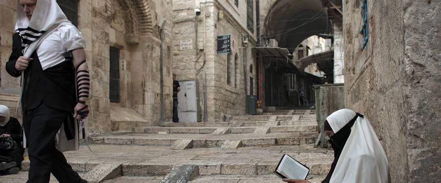 A Palestinian woman belonging to a group who call themselves Murabitat reads a copy of the Kuran, Islam's holy book, as a Jewish Orthodox man walks past her in Jerusalem's Old City on September 10, 2015.
