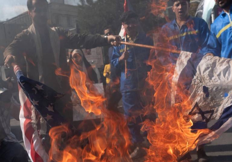 An Iranian protester wearing a military uniform burns the U.S. and Israeli flags during an anti-Israel rally in Tehran on Oct. 20, 2023