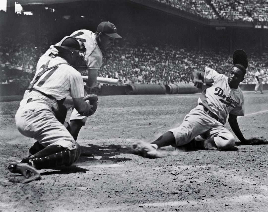 Jackie Robinson, of the Brooklyn Dodgers, slides home on a steal in the fourth inning of the first game of a doubleheader with the Phillies, July 2, 1954