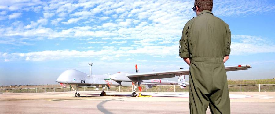 A soldier watches an Israeli IAI Heron TP drone on a tarmac. The IAI Heron TP is a multirole, advanced, long-range Medium Altitude Long Endurance, Unmanned Aerial System for strategic missions.