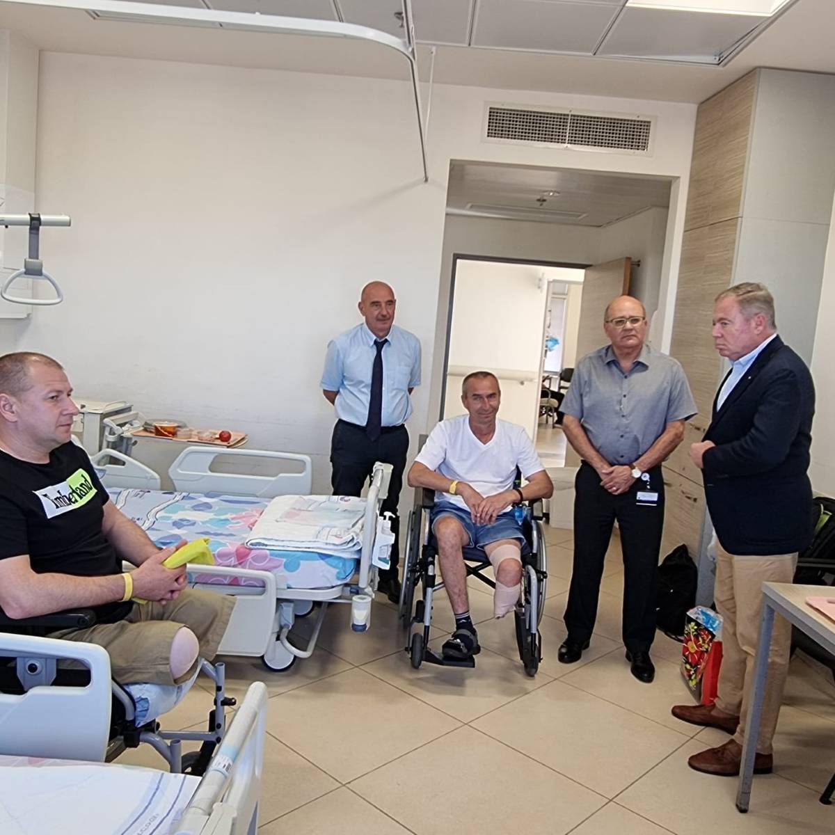 Ukraine Ambassador Korniychuk, at right wearing a jacket, meets at the Barzilai Medical Center in November with patients Aleksander, at left, and Piotr. Also in attendance are the hospital's CEO, Chezy Levy, center, and rehab department head Dr. Michael Warschavsky, left.