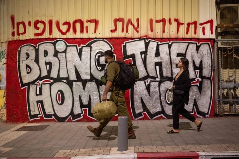 An IDF reservist walks past 'Bring Them Home Now' street art in the Florentin neighborhood of Tel Aviv on Nov. 16, 2023