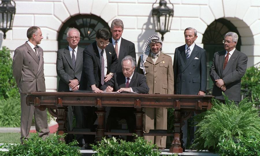 Israeli Foreign Minister Shimon Peres, seated at center, signs the historic Israel-PLO Oslo Accords on Palestinian autonomy in the occupied territories in a ceremony at the White House on Sept. 13, 1993. Others, from left, are Russian Foreign Minister Andrei Kozyrev, Israeli Prime Minister Yitzhak Rabin, unidentified aide, U.S. President Bill Clinton, PLO Chairman Yasser Arafat, U.S. Secretary of State Warren Christopher, and PLO political director Mahmoud Abbas. 