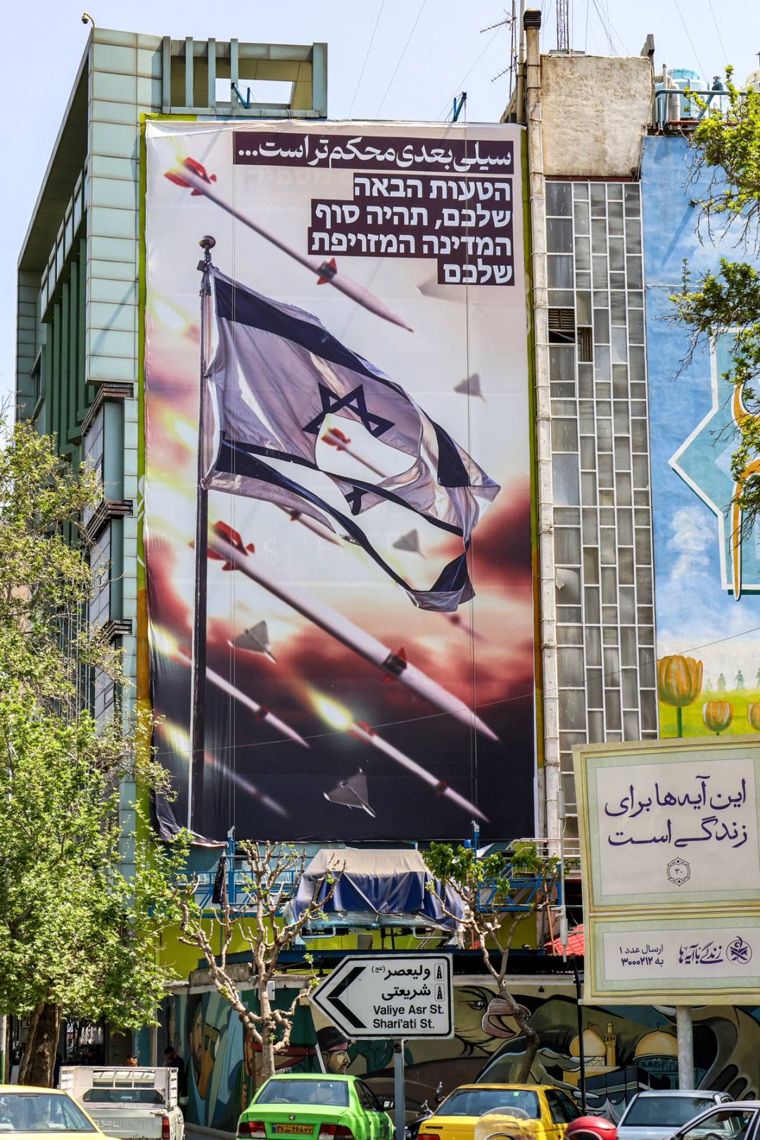 A banner depicting missiles and drones flying past a torn Israeli flag hangs on the facade of a building in Tehran’s Palestine Square, on April 14, 2024. The text in Persian reads ‘the next slap will be harder’ and in Hebrew ‘your next mistake will be the end of your fake state.’