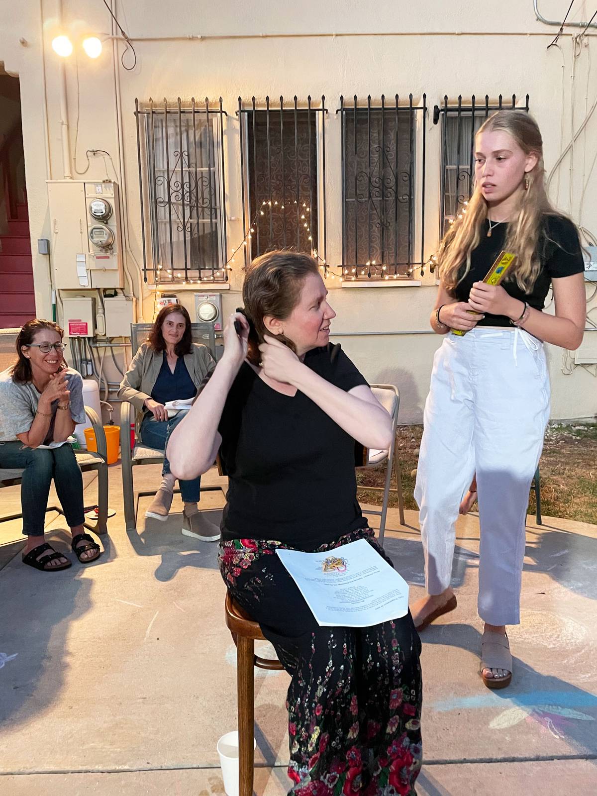The author, seated, prepares for her daughter to cut her hair during the ceremony, as friends look on