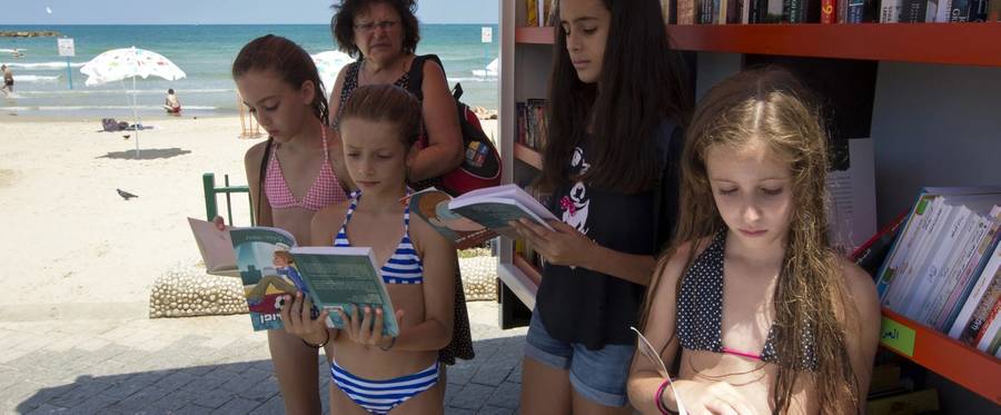 Israelis and foreign tourists read books from a multilingual mobile beach library in the Mediterranean coastal city of Tel Aviv on July 9, 2013. 