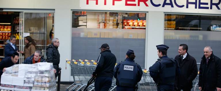 Police officers look on as employees and staff of the Hyper Cacher kosher supermarket worked to re-open the store in France, March 15, 2015. 