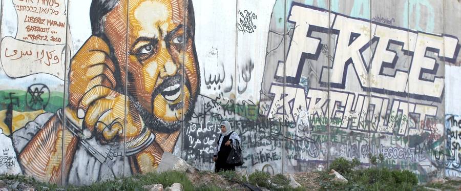 A Palestinian woman walks past a graffiti-covered section of the controversial Israeli separation wall showing jailed Fatah leader Marwan Barghuti at the Qalandia checkpoint in the Israeli occupied West Bank, April 5, 2014,