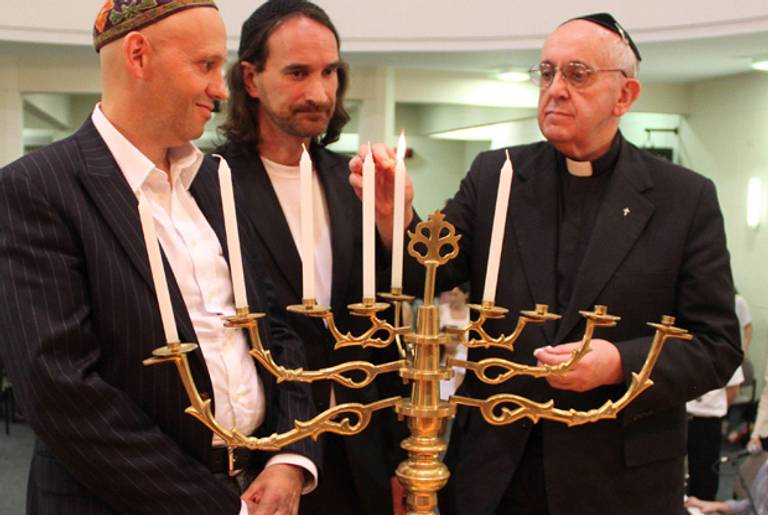 In this Dec. 12, 2012, picture provided by the NCI-Emanue El, Archbishop of Buenos Aires, Cardinal Jorge Mario Bergoglio (now Pope Francis), lights the menorah during Hanukkah celebrations in Buenos Aires, Argentina. At left is Rabbi Sergio Bergman, and at right is Rabbi Alejandro Avruj. (NCI-Emanu El/AP)