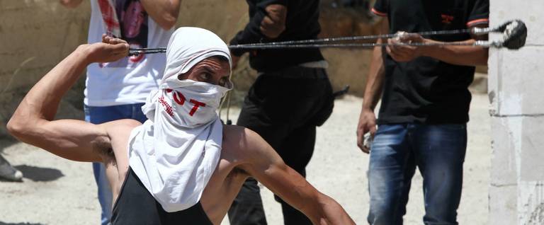 Using a slingshot, a Palestinian protester throw stones towards members of the Israeli security forces during clashes following the funeral of Falah Abu Maria, a 50-year old Palestinian man who was shot dead by Israeli troops during an arrest operation at his house in the village of Beit Omar, near the southern city of Hebron, on July 23, 2015.  