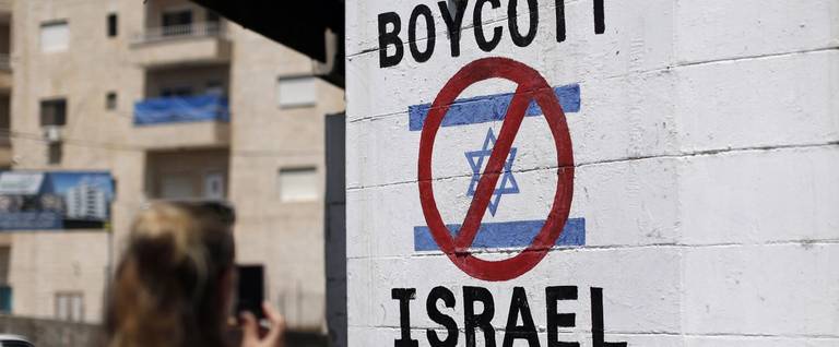 A tourist photographs a sign painted on a wall in the West Bank biblical town of Bethlehem on June 5, 2015, calling to boycott Israeli products coming from Jewish settlements. The international BDS (boycott, divestment and sanctions) campaign, that pushes for a ban on Israeli products, aims to exert political and economic pressure over Israel's occupation of the Palestinian territories in a bid to repeat the success of the campaign which ended apartheid in South Africa.