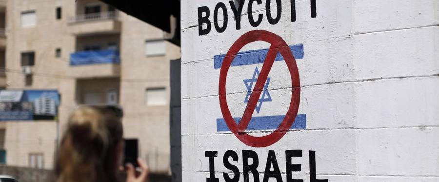 A tourist photographs a sign painted on a wall in the West Bank biblical town of Bethlehem on June 5, 2015, calling to boycott Israeli products coming from Jewish settlements. The international BDS (boycott, divestment and sanctions) campaign, that pushes for a ban on Israeli products, aims to exert political and economic pressure over Israel's occupation of the Palestinian territories in a bid to repeat the success of the campaign which ended apartheid in South Africa.