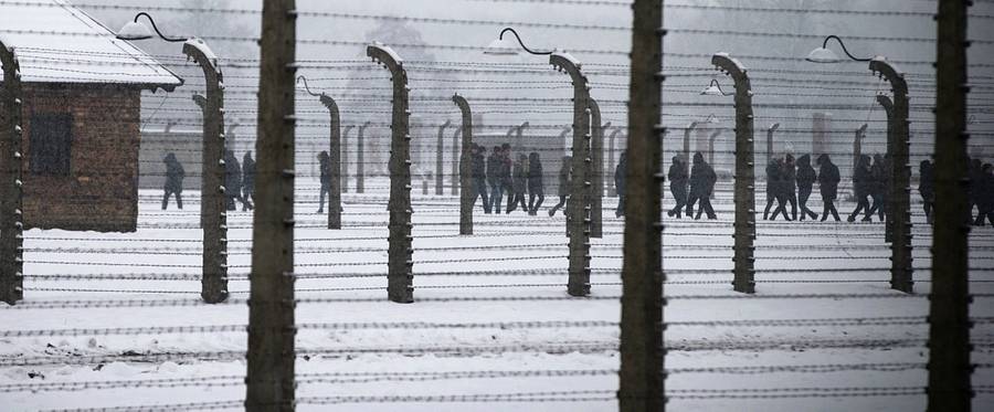 People walk behind barbed wire fences as they visit the memorial site of the former Nazi concentration camp Auschwitz-Birkenau in Oswiecim, Poland, on January 25, 2015.
