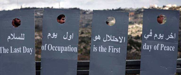 Israeli and Palestinian peace activists walk behind cardboard cutouts depicting the controversial Israeli separation barrier as they wave a Palestinian national flag during a peace march at an Israeli road near a checkpoint between the West Bank city of Beit Jala and Jerusalem on Jan. 15, 2016.