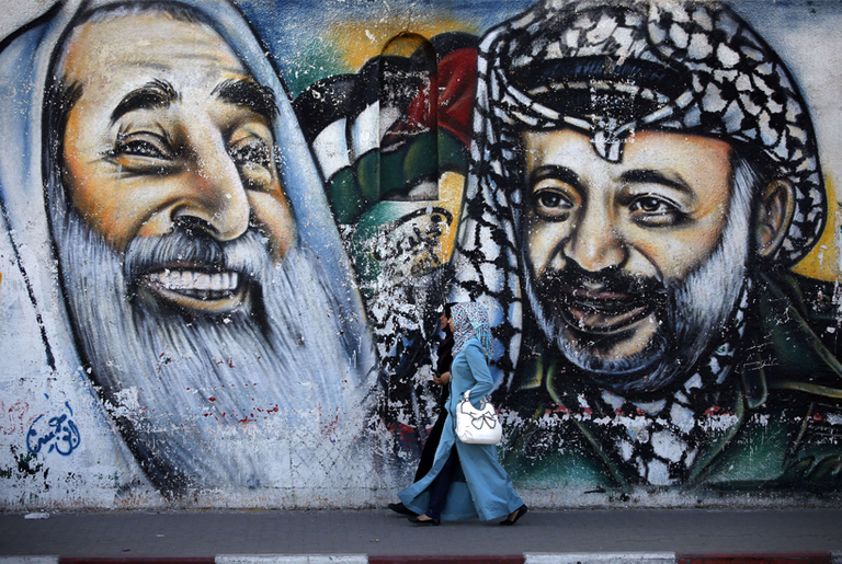 Palestinian women walk past a mural depicting late Hamas spiritual leader Sheikh Ahmed Yassin (L) and late Palestinian leader Yasser Arafat on May 4, 2014 in Gaza City.(Thomas Coex/AFP/Getty Images)