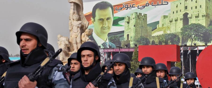 Syrian soldiers march in formation past a banner depicting President Bashar al-Assad on December 21, 2017