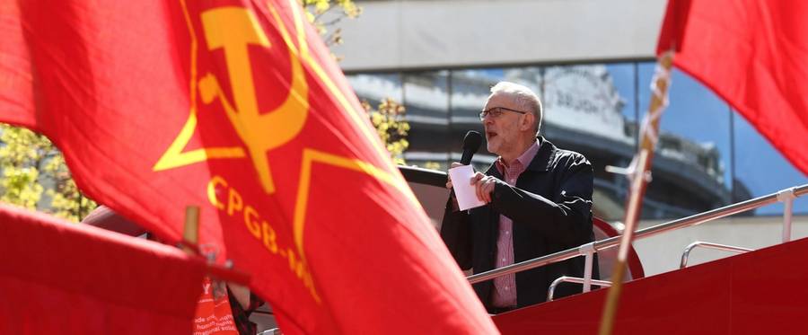 Britain's opposition Labour Party leader Jeremy Corbyn gives a speech from the top of a double-decker bus as Communist Party of Great Britain (Marxist-Leninist) flags fly at a May Day rally in London, England, May 1, 2016. 