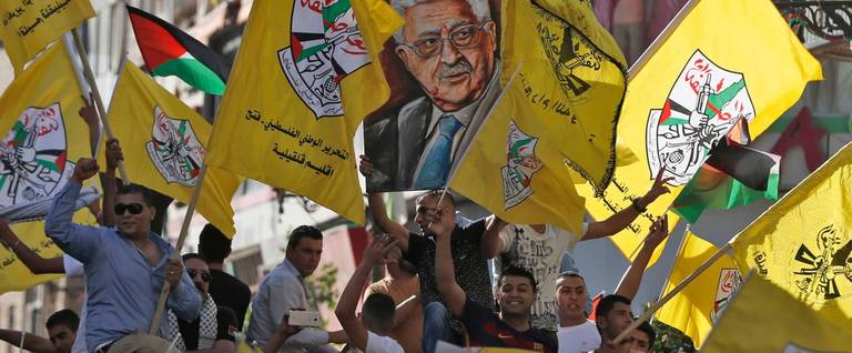 Palestinians supporting the Fatah movement wave both their national and the movement's flags as they take part in a demonstration in the West Bank city of Ramallah on October 4, 2016 in support of president Mahmud Abbas' participation in the funeral ceremony of former Israeli President Shimon Peres earlier in the week.